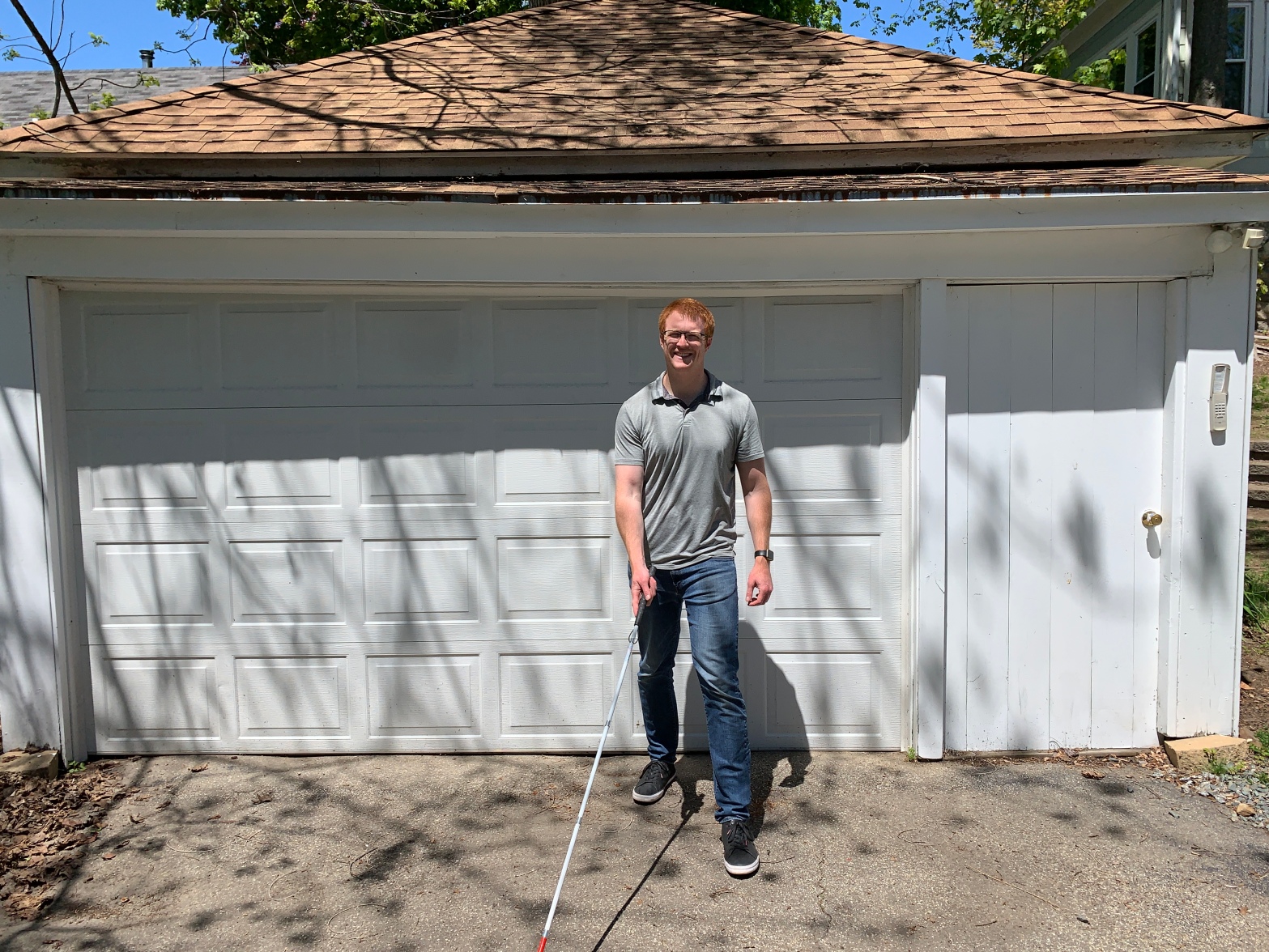 man with grey shirt and blue pants walking with a white cane